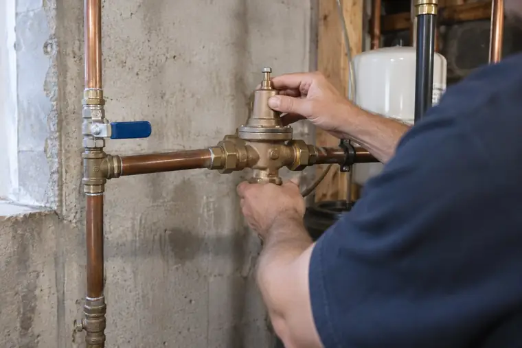 Plumber adjusting a brass pressure reducing valve on a basement main line